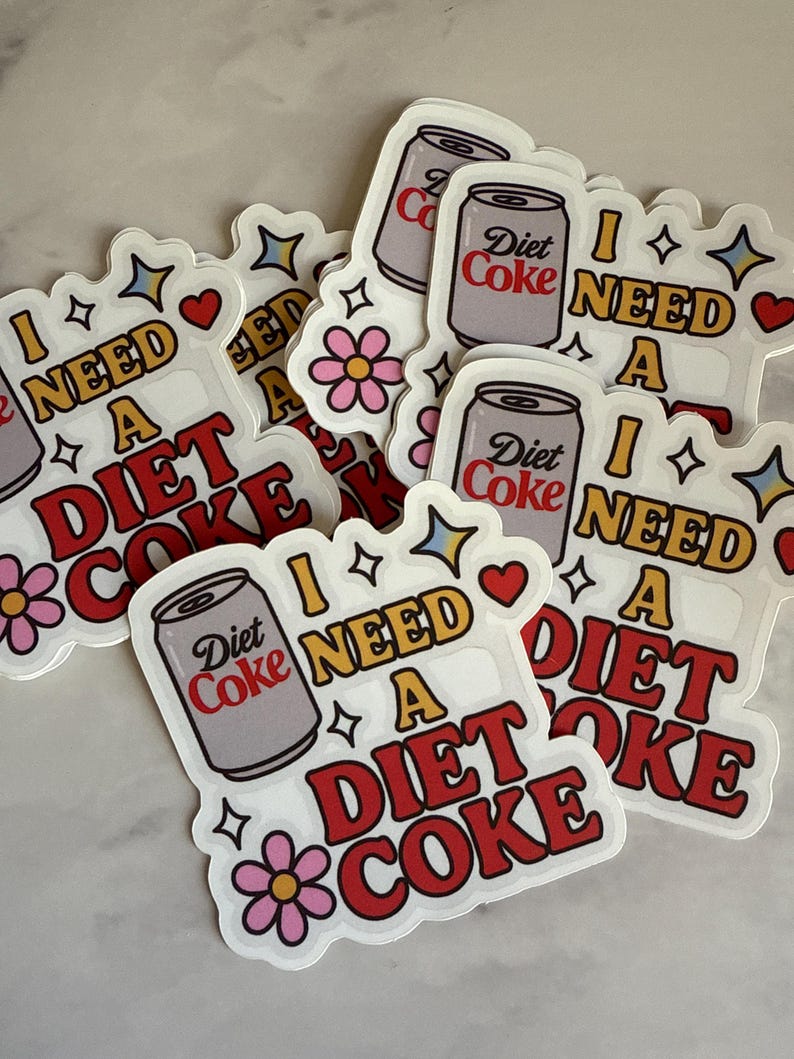 May include: A collection of stickers with a retro design. Each sticker features a Diet Coke can illustration and the phrase "I NEED A DIET COKE" in red and white lettering. Decorative elements include stars, hearts, and flowers.
