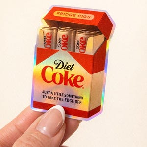 K&ouml;nnte beinhalten: Ein Aufkleber mit einer Diet Coke-Schachtel mit dem Text "FRIDGE CIGS". Die Schachtel enth&auml;lt drei Diet Coke-Dosen. Der Text "JUST A LITTLE SOMETHING TO TAKE THE EDGE OFF" ist ebenfalls sichtbar.