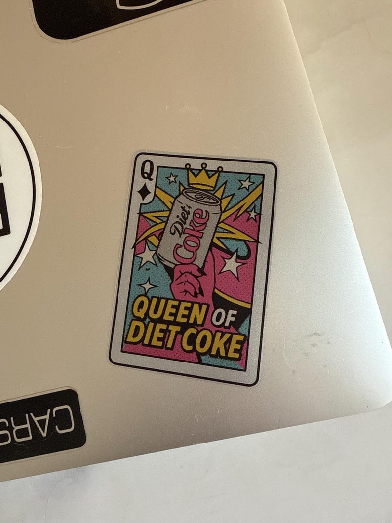 May include: A sticker featuring a playing card design with the text "Queen of Diet Coke." The card shows a Diet Coke can held by a hand, with a crown and starburst design. The card has a pink, blue, and yellow color scheme.