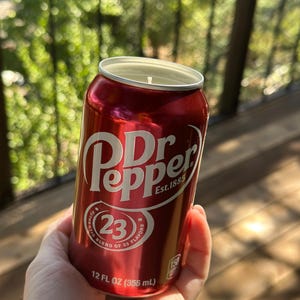 May include: A red aluminum can candle with a Dr Pepper label. The label features the Dr Pepper logo, the text "Est. 1885", and a circle with the number "23" and the text "Authentic Blend of 23 Flavors". The can is 12 fluid ounces (355 ml).