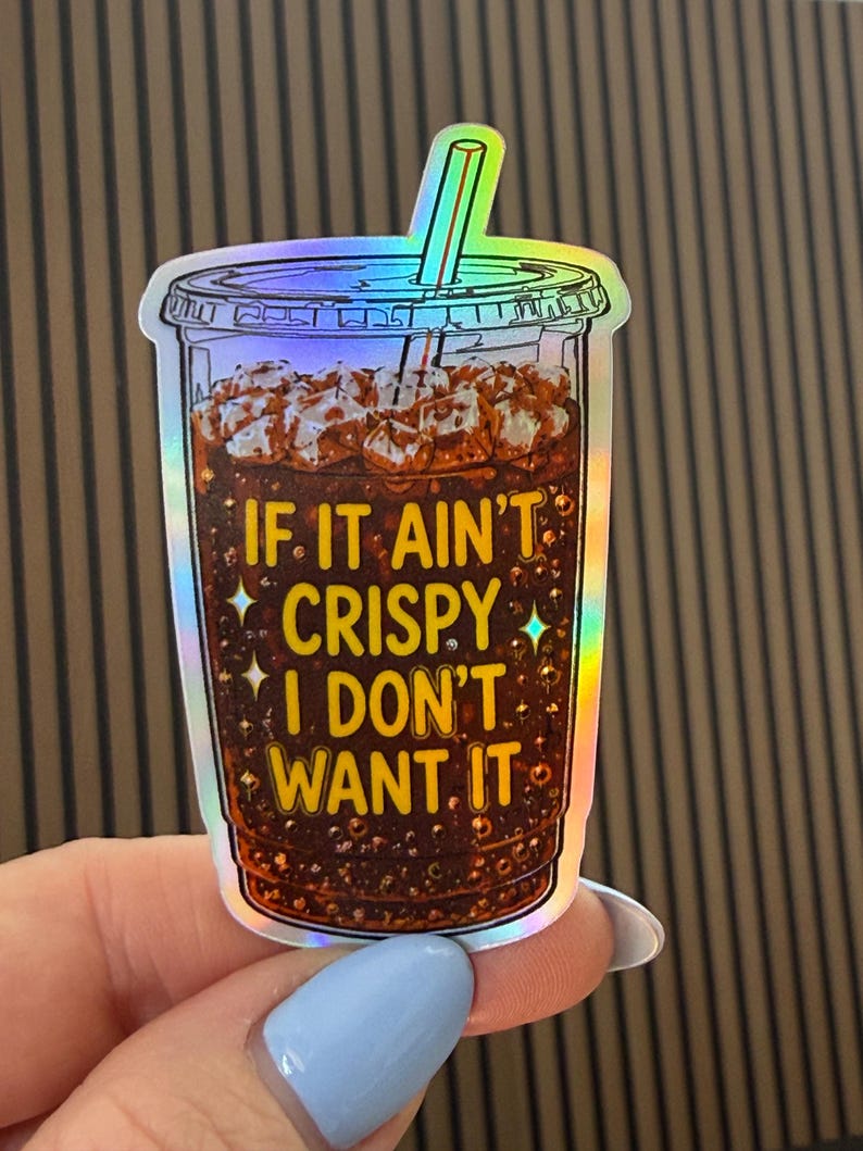 May include: A holographic sticker shaped like a plastic cup filled with a dark brown carbonated beverage, ice cubes, and a straw. The text IF IT AIN'T CRISPY I DON'T WANT IT is printed in yellow letters on the front of the cup with small star accents.
