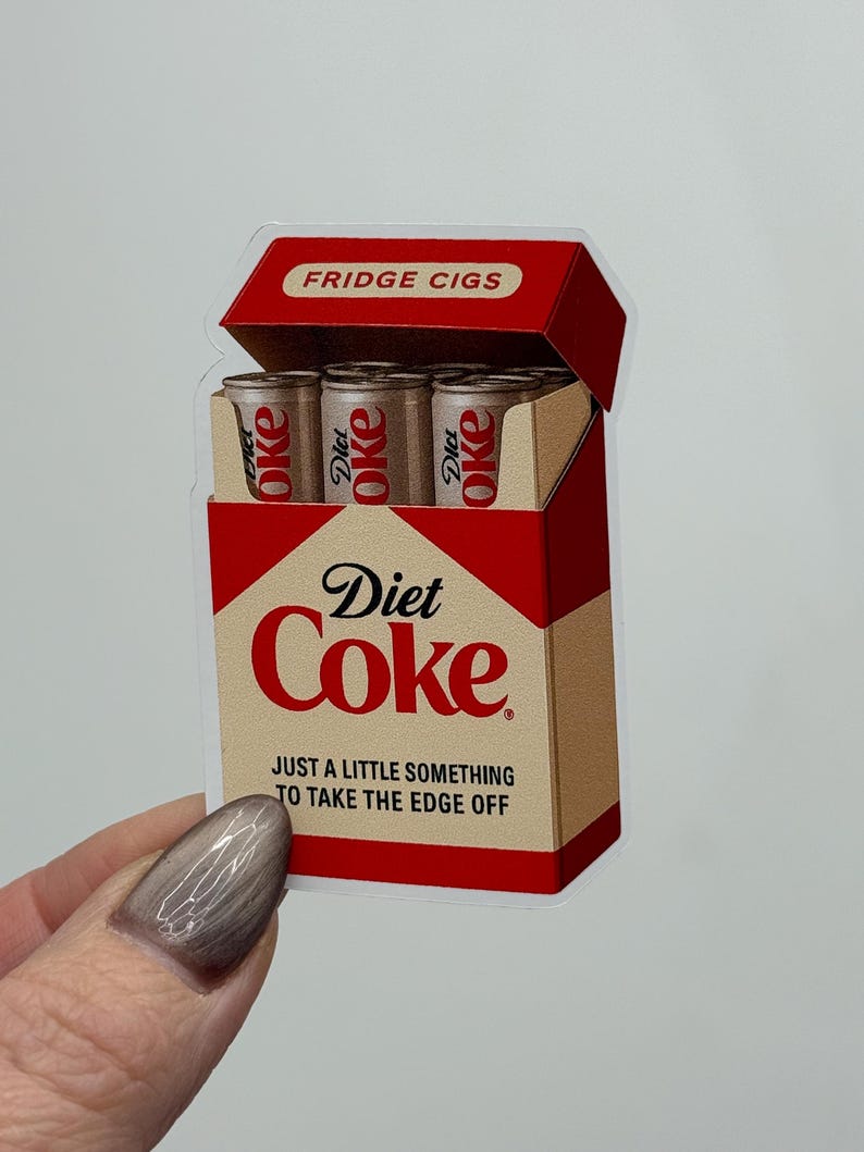 K&ouml;nnte beinhalten: Ein Aufkleber, der eine Diet Coke-Zigarettenschachtel darstellt. Die rote und beige Packung tr&auml;gt die Aufschrift "FRIDGE CIGS" und "Diet Coke". Im Inneren befinden sich drei Miniatur-Diet Coke-Dosen. Der Text "JUST A LITTLE SOMETHING TO TAKE THE EDGE OFF" ist ebenfalls sichtbar.