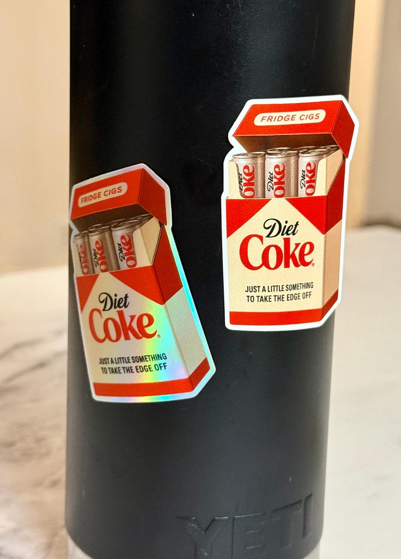 K&ouml;nnte beinhalten: Zwei Aufkleber mit einem Retro-Design, das einer Zigarettenschachtel &auml;hnelt, mit der Aufschrift "Fridge Cigs" und "Diet Coke". Die Aufkleber zeigen eine rot-wei&szlig;e Verpackung mit dem Markennamen "Diet Coke" und dem Satz "Nur ein kleines bisschen, um die Kanten abzurunden."