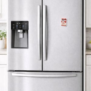K&ouml;nnte beinhalten: Ein K&uuml;hlschrank aus Edelstahl mit einem rot-wei&szlig;en Coke-Magneten an der T&uuml;r. Der K&uuml;hlschrank hat einen Wasser- und Eisspender und eine untere Gefrierschublade. Die Griffe sind silberfarben.