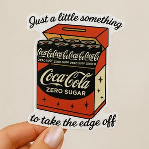 May include: A sticker featuring a retro-style Coca-Cola Zero Sugar box with six cans inside. The box is red and black with the Coca-Cola logo. Text on the sticker reads "Just a little something to take the edge off."