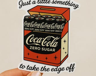May include: A sticker featuring a retro-style Coca-Cola Zero Sugar box with six cans inside. The box is red and black with the Coca-Cola logo. Text on the sticker reads "Just a little something to take the edge off."