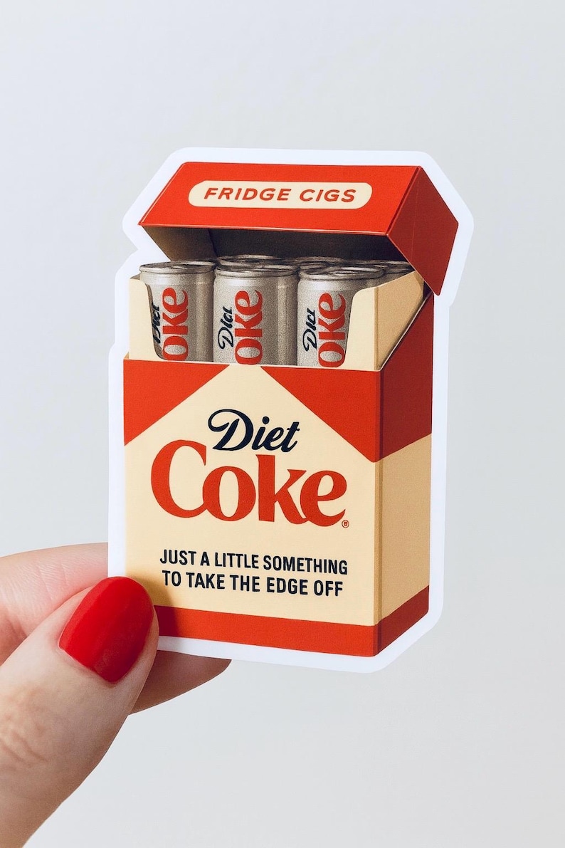 May include: A sticker resembling a cigarette pack, labeled "FRIDGE CIGS." The pack is red and beige, with "Diet Coke" branding. Inside are three miniature Diet Coke cans. The text "JUST A LITTLE SOMETHING TO TAKE THE EDGE OFF" is also visible.