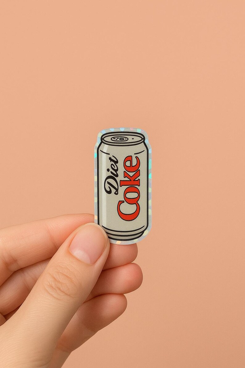 May include: A Diet Coke sticker in a can shape. The can is silver with the words "Diet Coke" in black and red. The sticker has a holographic, iridescent finish.