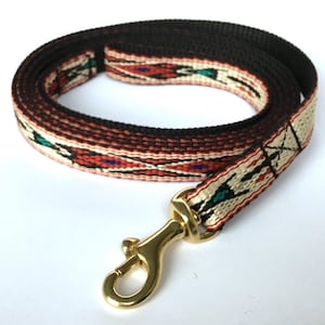 May include: A black and red patterned dog leash with a gold metal clip. The leash is made of woven fabric with a geometric design.