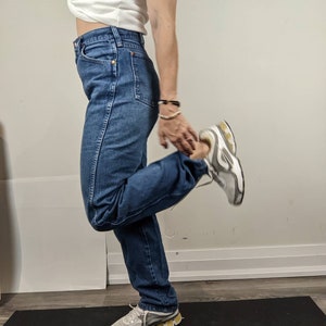 May include: A person wearing blue denim jeans with a white shirt and white sneakers. The person is standing on a black yoga mat.