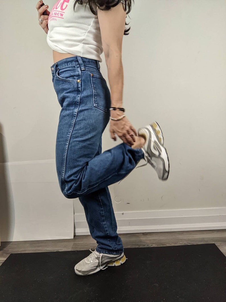 May include: A person wearing blue denim jeans with a white shirt and white sneakers. The person is standing on a black yoga mat.