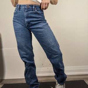 May include: A pair of blue denim jeans with a high waist and a straight leg fit. The jeans have a classic five-pocket style and a button fly.