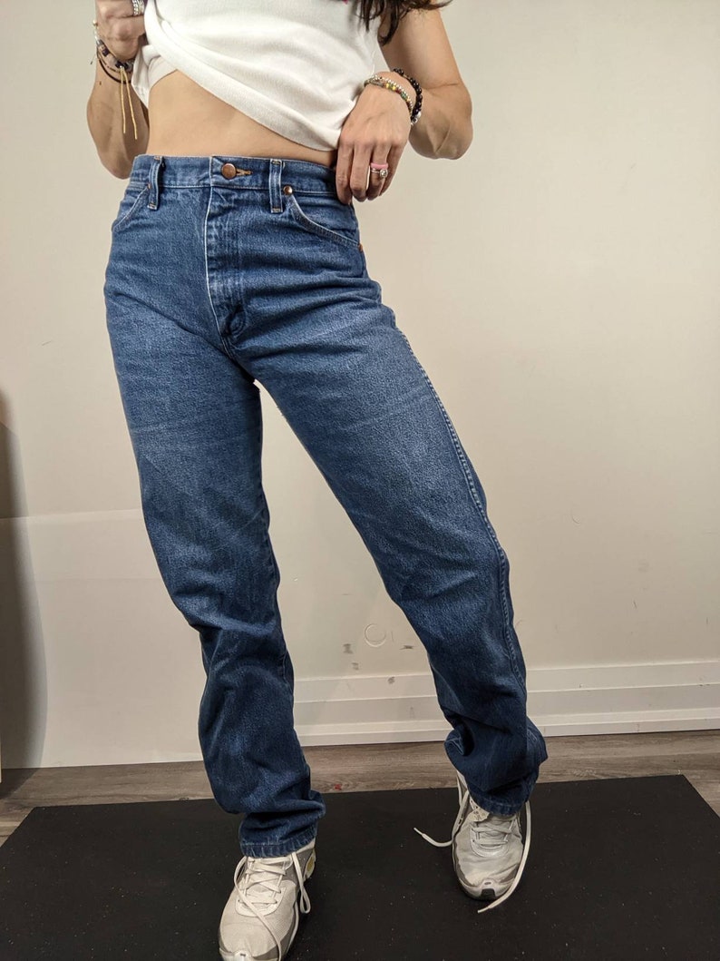 May include: A pair of blue denim jeans with a high waist and a straight leg fit. The jeans have a classic five-pocket style and a button fly.