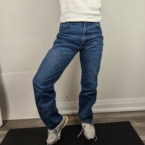May include: A person wearing a white t-shirt with the text "Capone's Dinner & Show Orlando, Florida" in pink lettering, blue jeans, and gray sneakers.