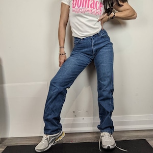 May include: A woman wearing a white t-shirt with a pink graphic that says "Dollface Capone's Dinner & Show Orlando, Florida" and blue jeans. She is wearing white sneakers.