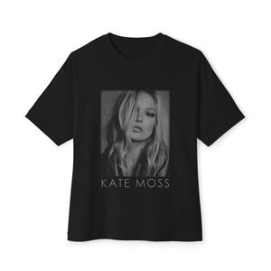 Può includere: T-shirt nero con un'immagine in bianco e nero di Kate Moss. Il ritratto mostra la modella con i capelli che le coprono parte del viso. Il testo "KATE MOSS" è stampato in bianco sotto.