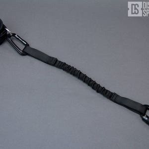 May include: A black elastic leash with a padded wrist strap and two metal carabiners.