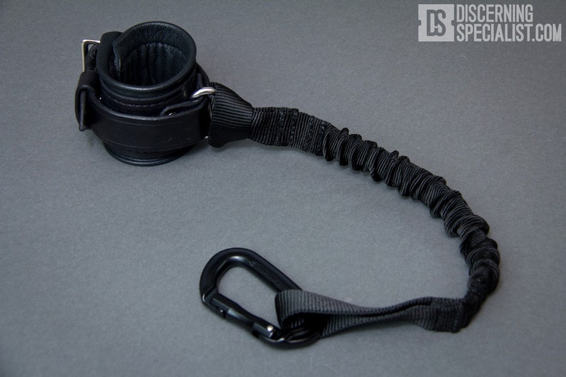 May include: Black leather wrist cuff with a black elastic strap and a black carabiner clip.