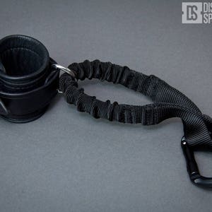 May include: Black leather cuff with a silver buckle and a black elastic strap with a black carabiner clip.