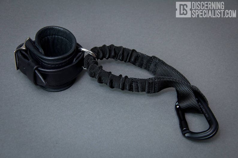 May include: Black leather cuff with a silver buckle and a black elastic strap with a black carabiner clip.