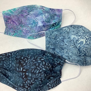 May include: Three blue and white patterned face masks with white elastic ear loops. The masks are made of fabric and have a pleated design.