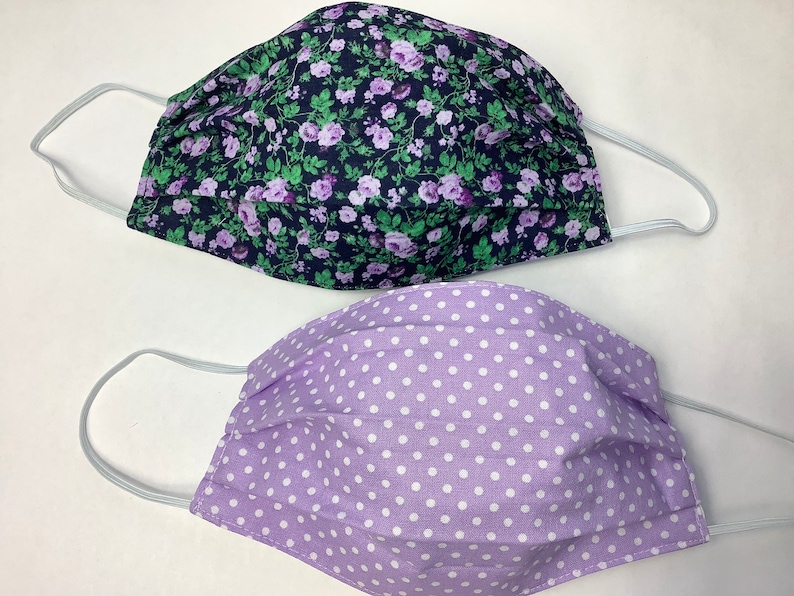 May include: Two fabric face masks. One mask is purple with white polka dots. The other mask is black with a floral pattern in shades of purple and green.