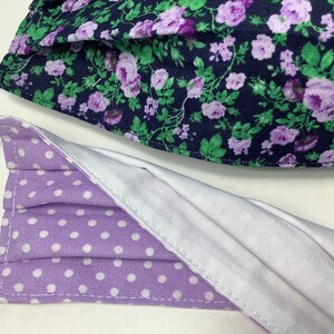 May include: Two face masks, one with a purple and white polka dot pattern and the other with a floral pattern featuring purple flowers on a dark blue background.