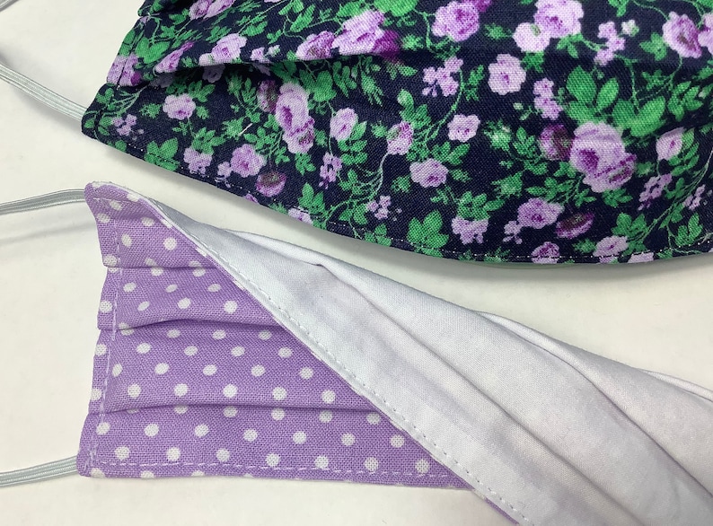 May include: Two face masks, one with a purple and white polka dot pattern and the other with a floral pattern featuring purple flowers on a dark blue background.