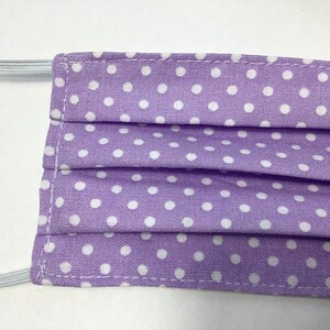 May include: A purple face mask with white polka dots. The mask is pleated and has elastic ear loops.