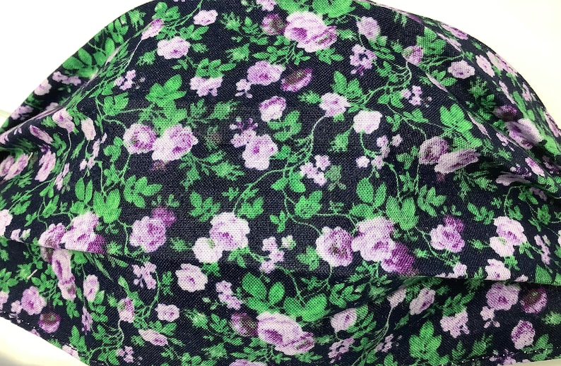 May include: A dark blue fabric face mask with a floral pattern featuring small purple and white flowers on green stems.