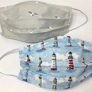 May include: Two fabric face masks. One mask is light gray with a white seagull pattern. The other mask is light blue with a white lighthouse pattern.