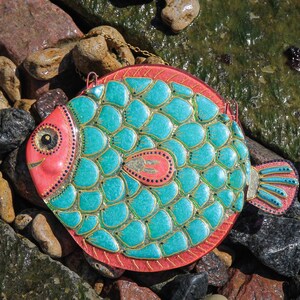 May include: A turquoise and pink fish-shaped wall hanging with gold accents. The fish has a scaly design and a large eye.