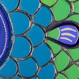 May include: Close-up of a colorful mosaic fish design with blue, green, and white scales. The fish has a large eye with white dots around the pupil.