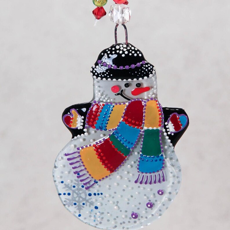 Pode incluir: Enfeite de Natal de boneco de neve com chap&eacute;u preto e cachecol colorido. O boneco de neve tem um nariz vermelho e um cachecol com listras azuis, verdes, amarelas e vermelhas. O enfeite &eacute; decorado com pontos brancos e detalhes roxos.