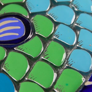 May include: Close-up of a mosaic-style fish sculpture with blue, green, and white scales. The fish has a blue eye with a white pupil and a white line across the eye.