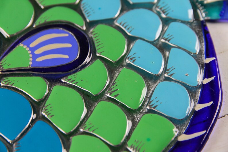 May include: Close-up of a mosaic-style fish sculpture with blue, green, and white scales. The fish has a blue eye with a white pupil and a white line across the eye.