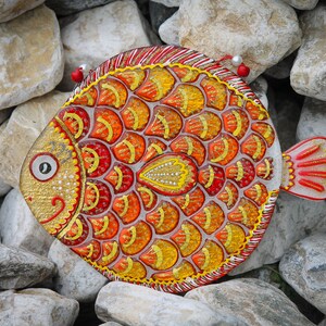 May include: A colorful, hand-painted fish ornament with red, orange, and yellow scales. The fish is made of glass and has a shiny, glittery finish.