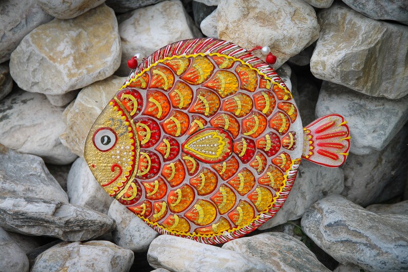 May include: A colorful, hand-painted fish ornament with red, orange, and yellow scales. The fish is made of glass and has a shiny, glittery finish.