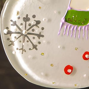 May include: A white glass ornament with a silver snowflake design, red and white dots, and a purple and green design at the top.