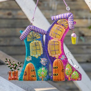 May include: Two whimsical glass houses with colorful paint and details, including windows, doors, and flowers. The houses are connected and hang from a string.