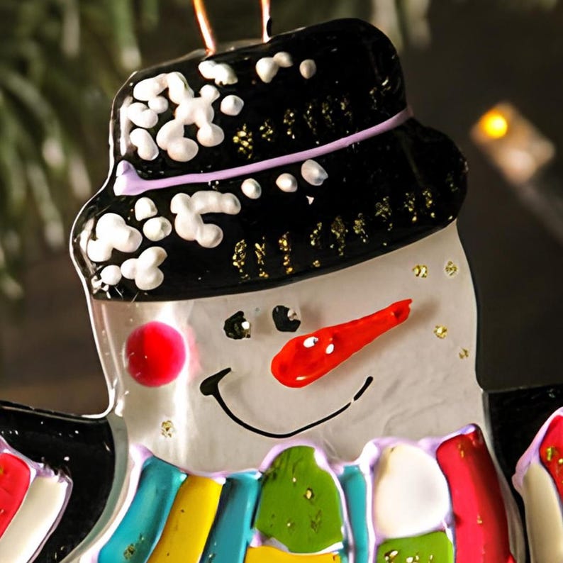 May include: A glass snowman ornament with a black hat, white trim, and a red nose. The snowman is wearing a colorful scarf and has a painted smile.