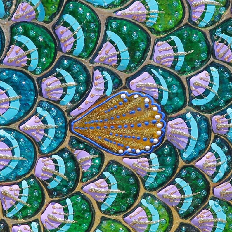 May include: Close-up of a mosaic art piece with a gold, blue, and white shell design. The background is made up of green, blue, and purple scales.