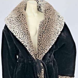 May include: A black faux fur robe with a shawl collar and cuffs featuring a leopard print pattern. The robe has a matching tie belt and a tassel. The robe is displayed on a mannequin.