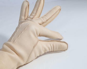 May include: A pair of light beige leather gloves. The gloves have a classic design with visible stitching along the seams and a slightly textured appearance. The fingers are well-defined, and the overall style suggests a focus on comfort and durability.