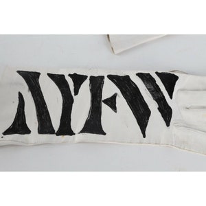 May include: A white leather glove with the word "NEW" written in black paint across the back of the hand.