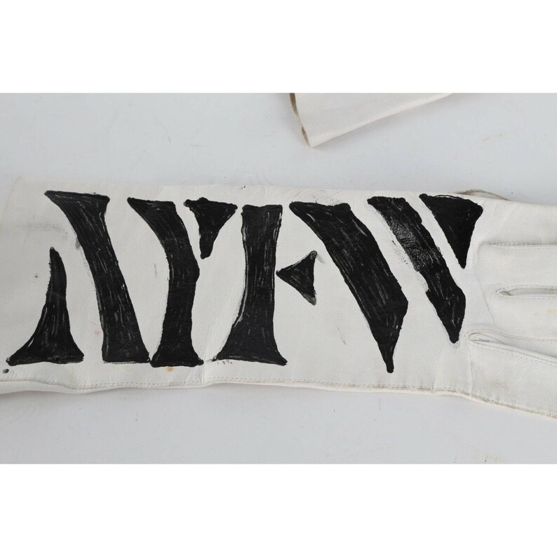 May include: A white leather glove with the word "NEW" written in black paint across the back of the hand.