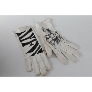 May include: A pair of white leather gloves with black ink drawings. One glove has a zebra stripe pattern and the other has a drawing of a woman in a dress.