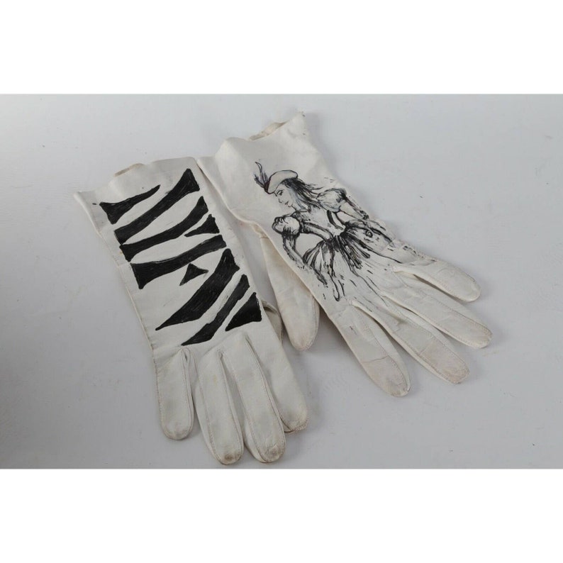 May include: A pair of white leather gloves with black ink drawings. One glove has a zebra stripe pattern and the other has a drawing of a woman in a dress.