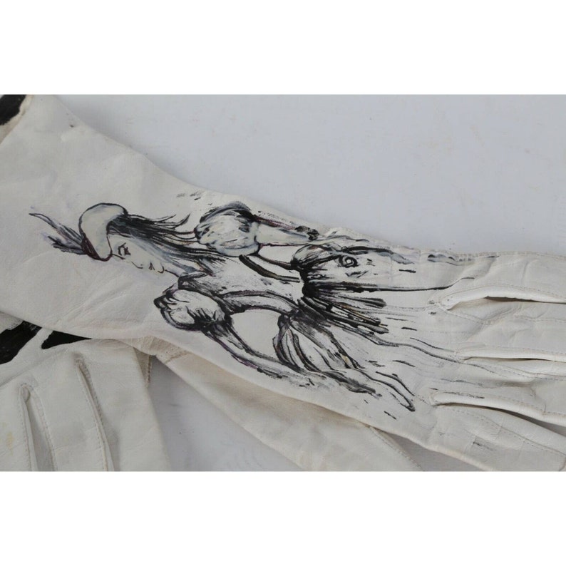 May include: A pair of white leather gloves with a black and white ink drawing of a woman in a dress on the back of one glove.