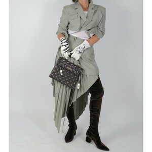 May include: A woman wearing a green cropped blazer, a white top, a green pleated skirt, and brown over-the-knee boots. She is carrying a brown quilted handbag with a gold clasp.